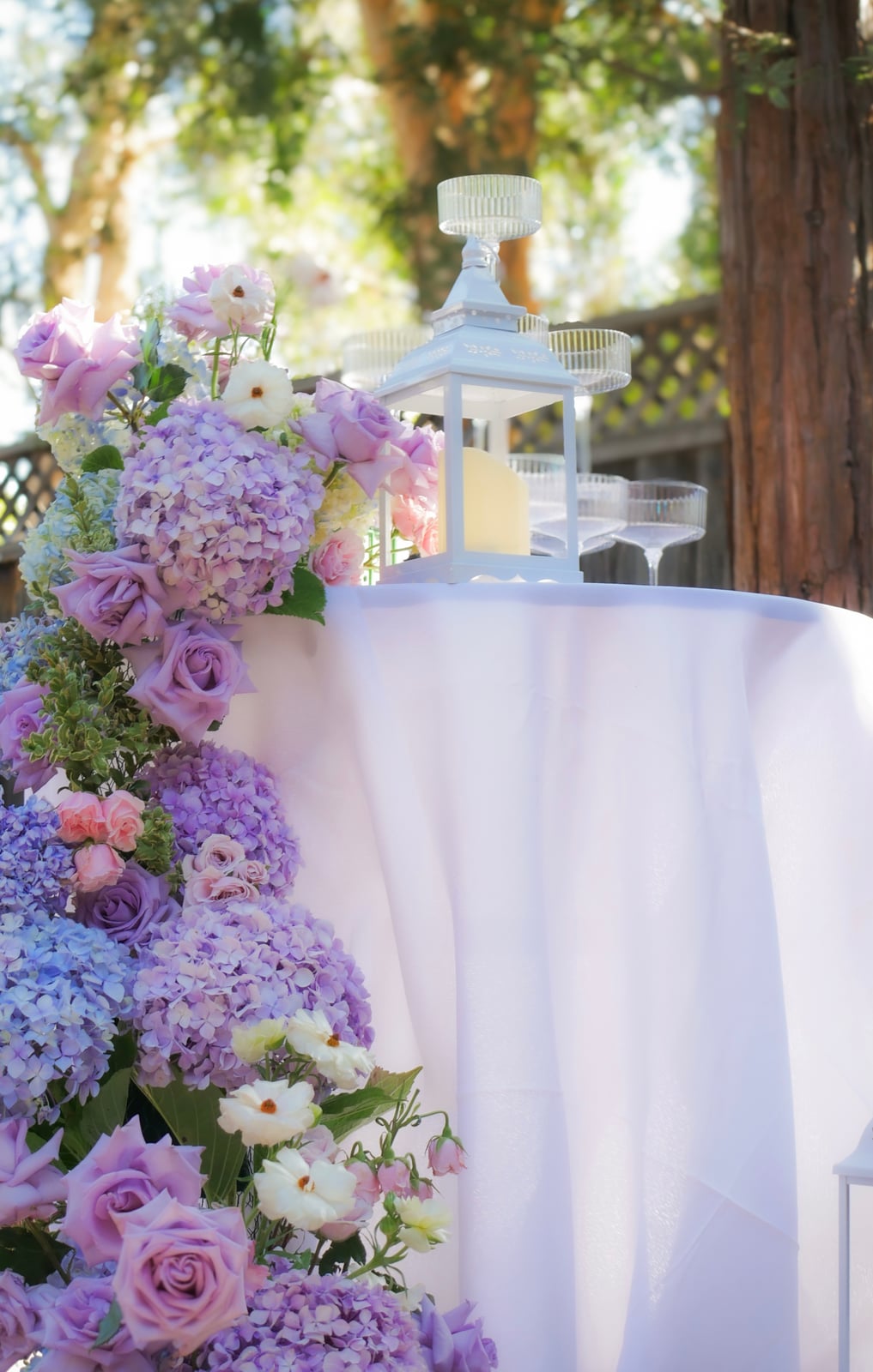 Lavender and ivory flowers beside a white lantern on an outdoor table