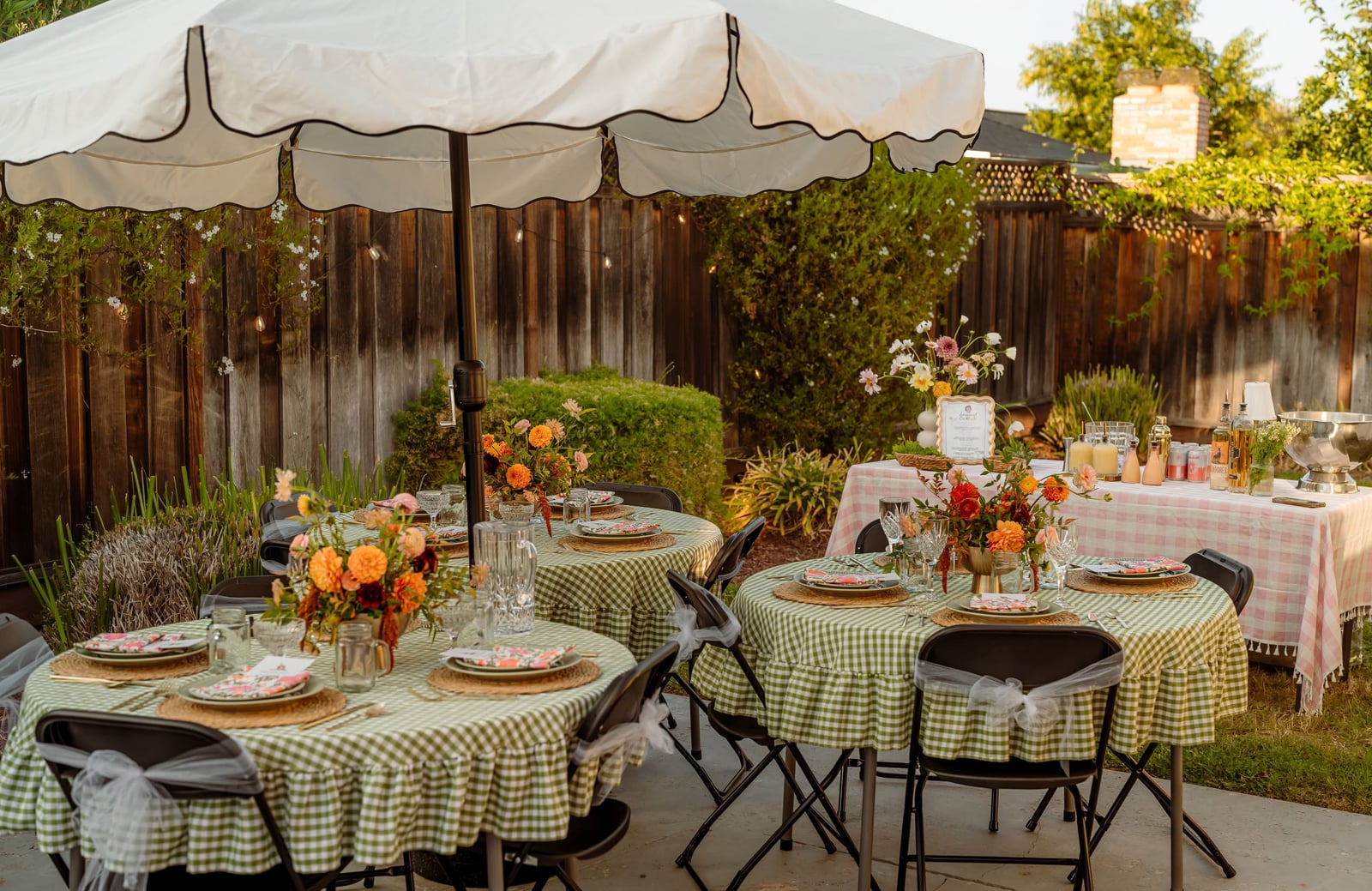Outdoor reception tables with garden-inspired centerpieces beneath umbrellas