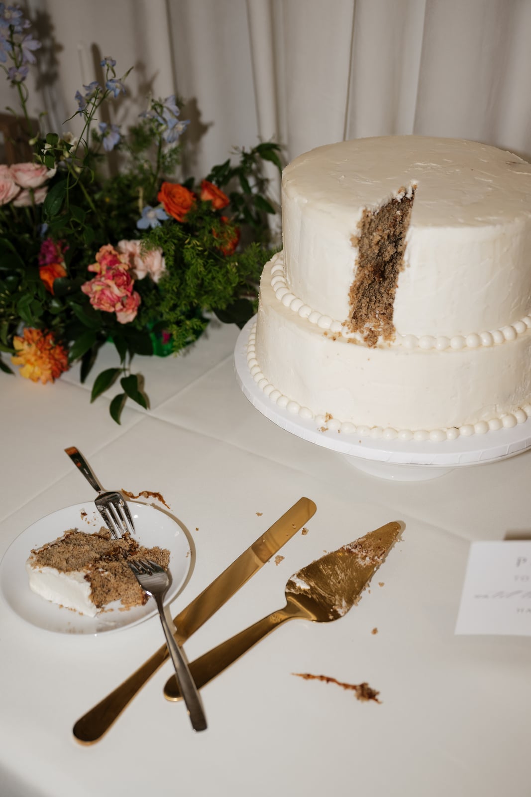 White tiered wedding cake beside colorful flowers